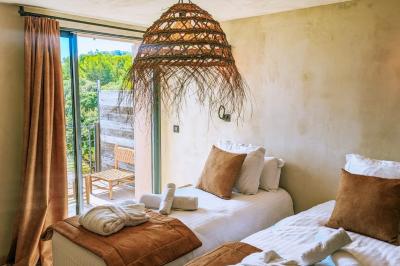 Chambre lumineuse avec lit double, oreillers et peignoirs, fenêtre donnant sur un jardin arboré.