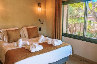 Chambre lumineuse avec lit double, oreillers et peignoirs, fenêtre donnant sur un jardin arboré.