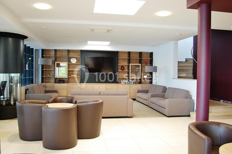 Salon moderne avec canapés beiges, fauteuils en cuir marron, étagères en bois et télévision murale.