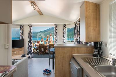 Intérieur d'un mobil-home lumineux avec cuisine équipée, vue sur une terrasse et paysage montagneux à l'extérieur.