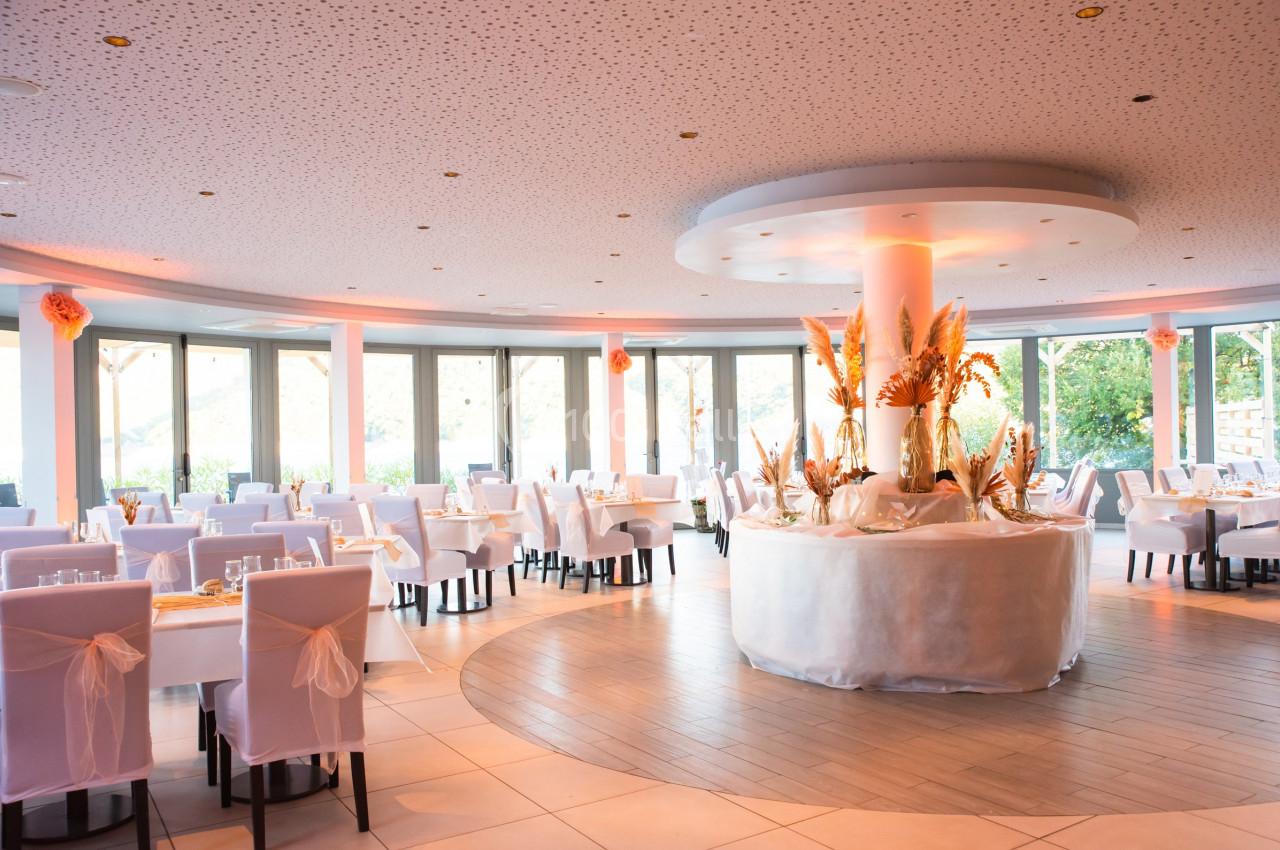 Salle de réception lumineuse avec des tables dressées et une décoration florale centrale sur une table ronde.