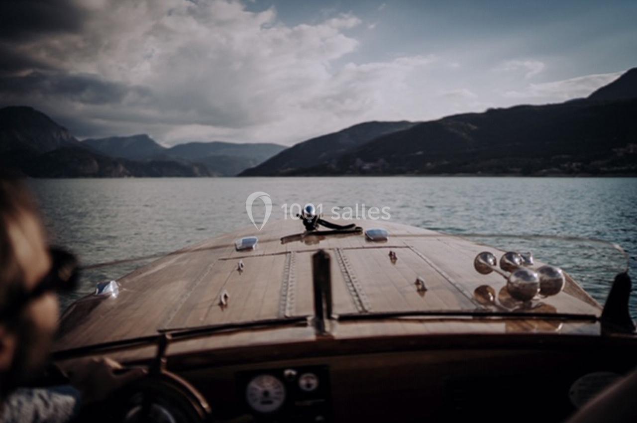 Vue depuis un bateau en bois naviguant sur un lac entouré de montagnes sous un ciel partiellement nuageux.