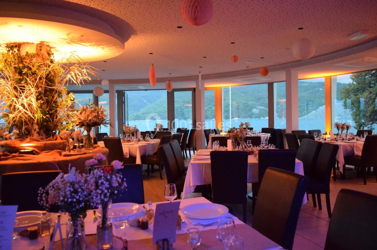 Salle de restaurant élégante avec tables dressées, éclairage chaleureux et vue sur un paysage lacustre.