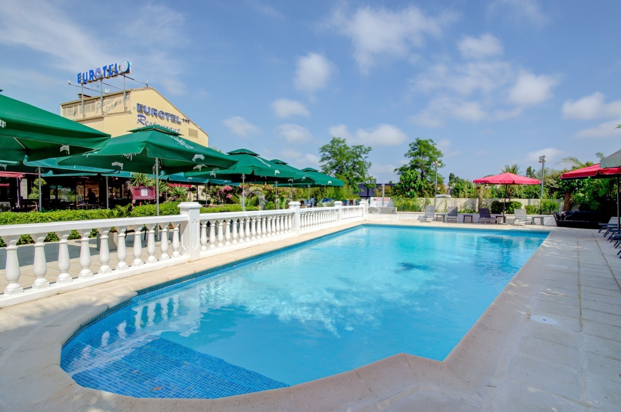 Piscine extérieure entourée de parasols verts, chaises longues et balustrades blanches, par temps ensoleillé.
