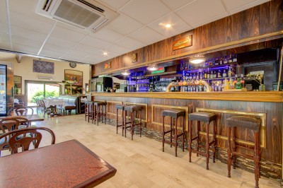 Intérieur d'un bar avec comptoir en bois, tabourets alignés, étagères de bouteilles et lumière tamisée.
