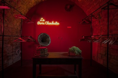 Fléchettes colorées dans une caisse en bois au premier plan, cible de jeu accrochée sur un mur en pierre en arrière-plan.