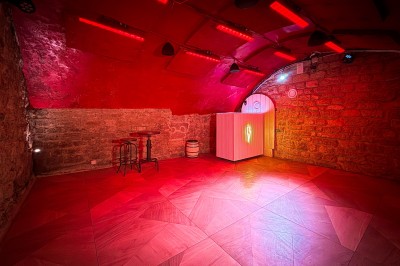 Fléchettes colorées dans une caisse en bois au premier plan, cible de jeu accrochée sur un mur en pierre en arrière-plan.