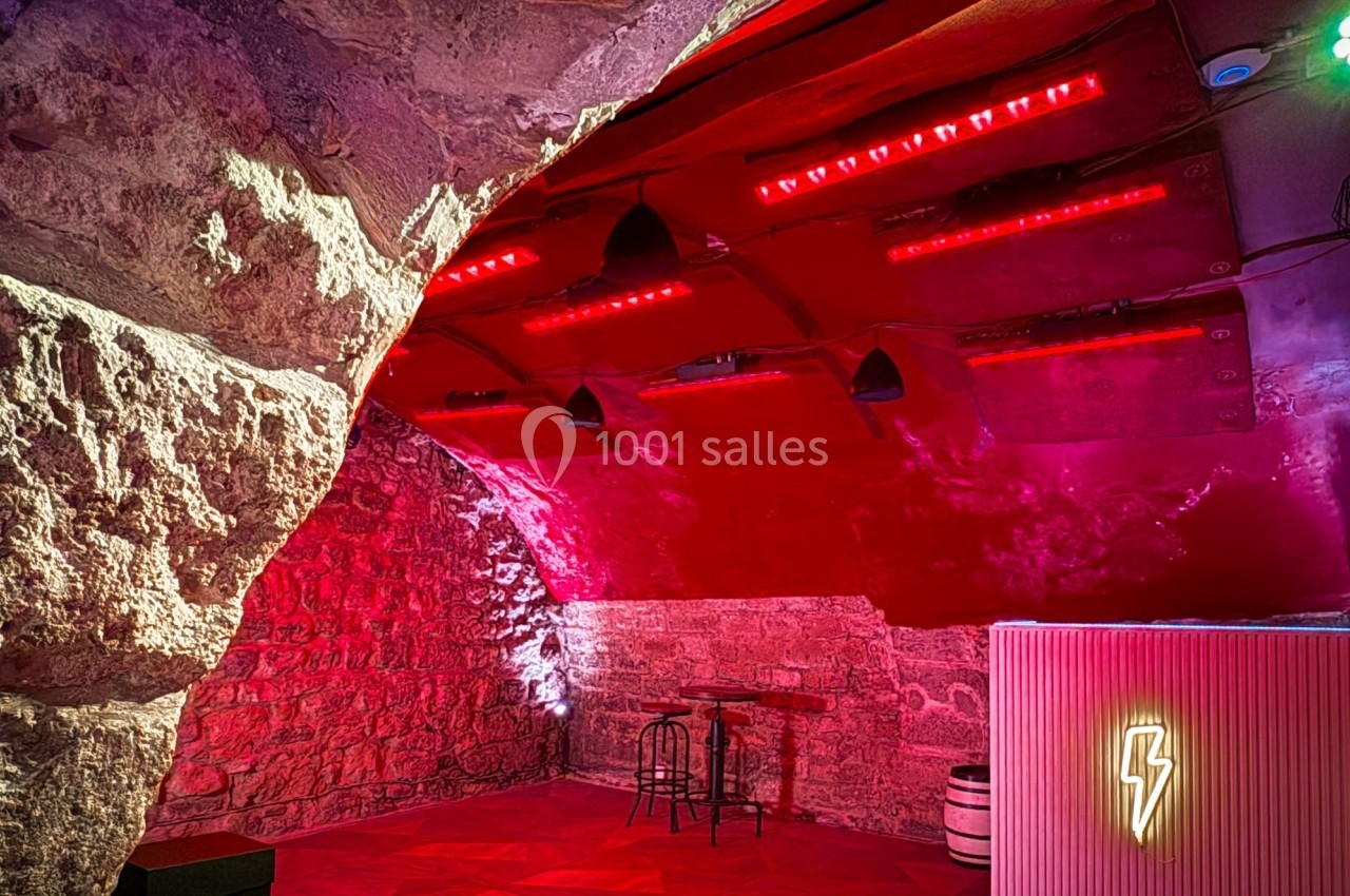 Salle voûtée en pierre avec éclairage rouge, un bar lumineux et quelques meubles minimalistes.
