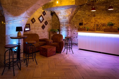 Fléchettes colorées dans une caisse en bois au premier plan, cible de jeu accrochée sur un mur en pierre en arrière-plan.