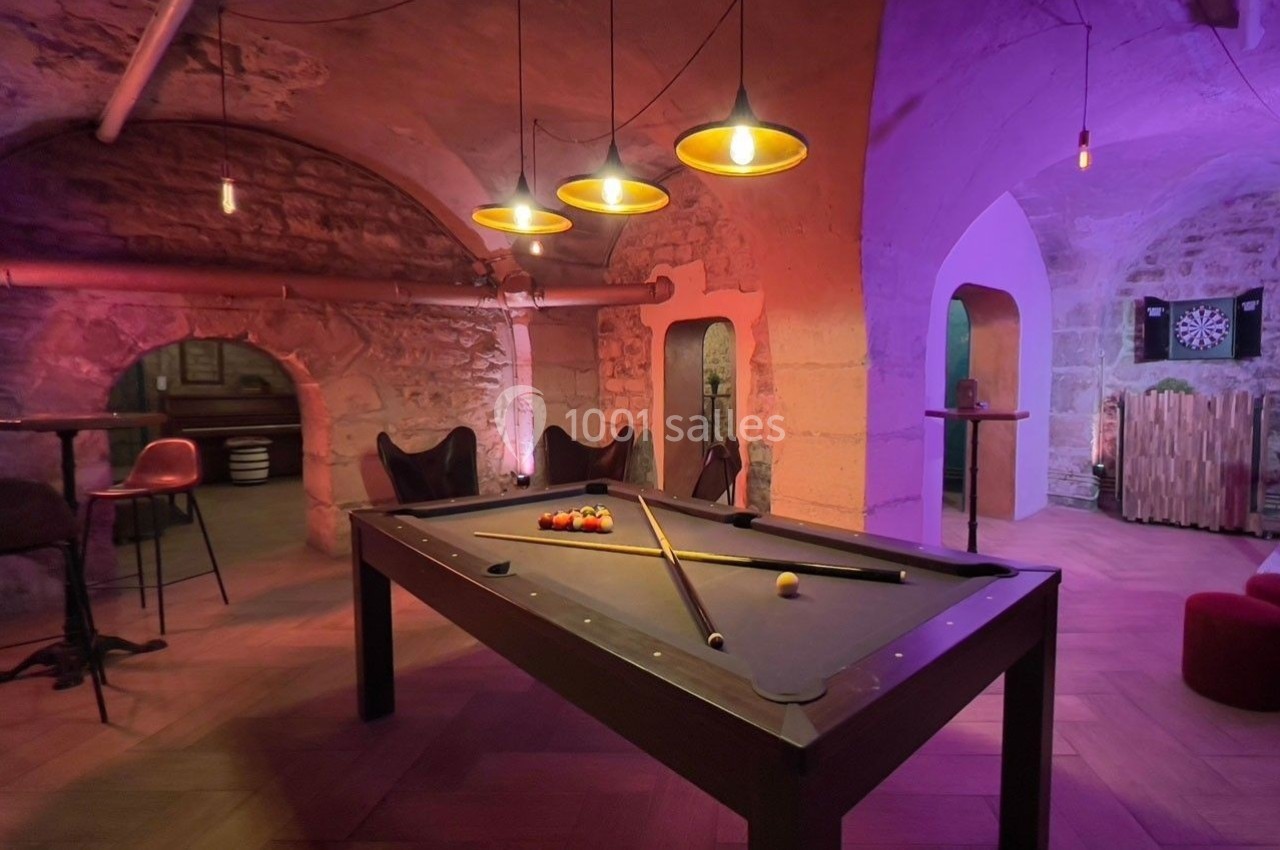 Table de billard dans une pièce voûtée en pierre, éclairée par des suspensions lumineuses et une ambiance tamisée.