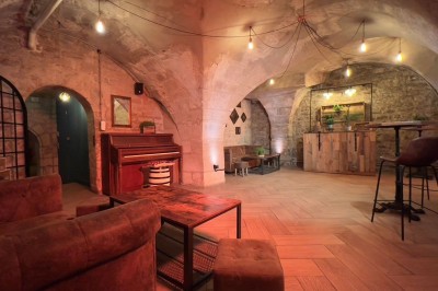 Fléchettes colorées dans une caisse en bois au premier plan, cible de jeu accrochée sur un mur en pierre en arrière-plan.