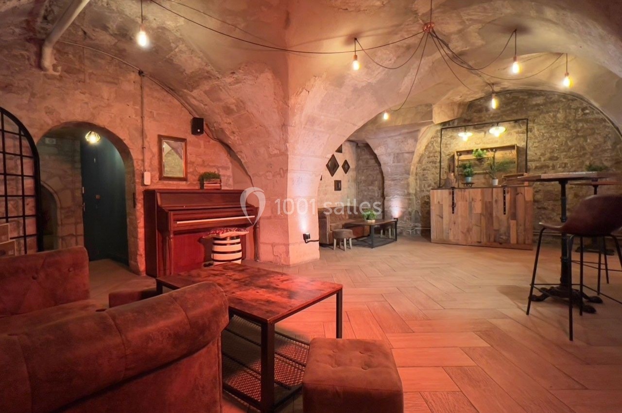 Salle voûtée en pierre avec éclairage chaleureux, mobilier en bois et cuir, piano et comptoir en arrière-plan.