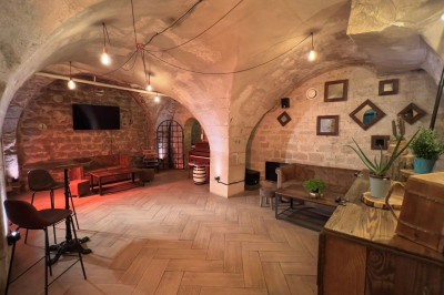 Fléchettes colorées dans une caisse en bois au premier plan, cible de jeu accrochée sur un mur en pierre en arrière-plan.