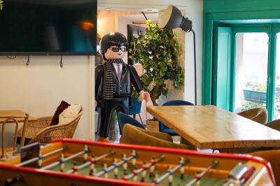 Salle lumineuse avec tables, chaises variées, baby-foot, miroir rond et murs en pierre apparente.