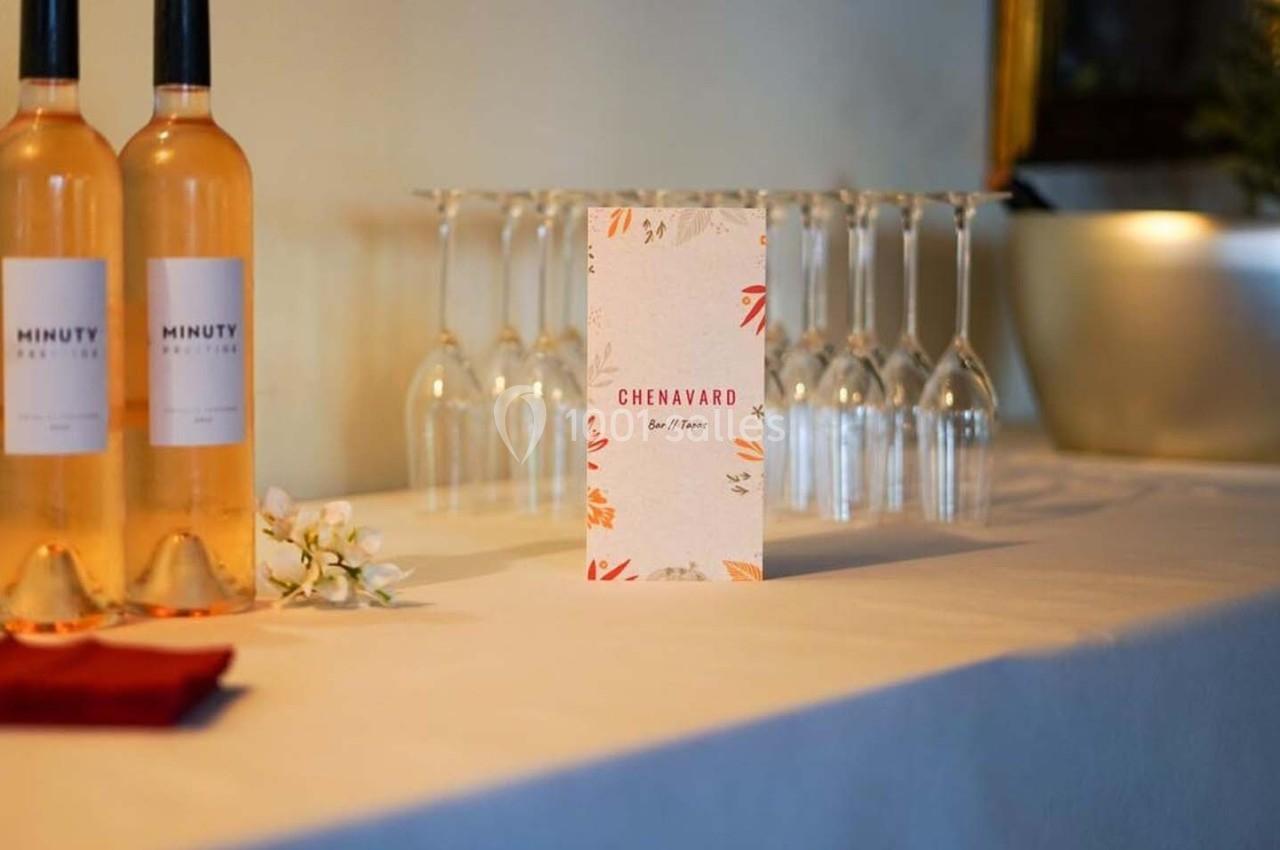 Bouteilles de vin rosé, verres à pied et menu disposés sur une table blanche dans un cadre élégant.