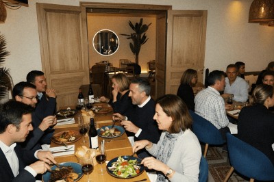 Salle lumineuse avec tables, chaises variées, baby-foot, miroir rond et murs en pierre apparente.