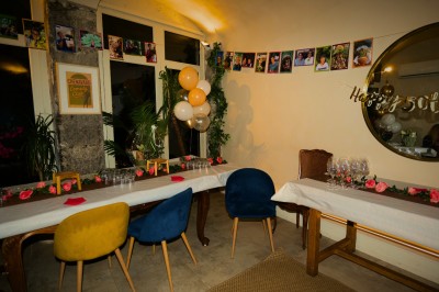 Salle lumineuse avec tables, chaises variées, baby-foot, miroir rond et murs en pierre apparente.