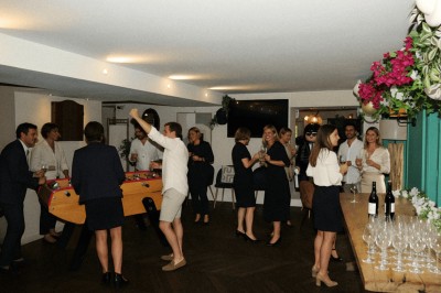 Salle lumineuse avec tables, chaises variées, baby-foot, miroir rond et murs en pierre apparente.