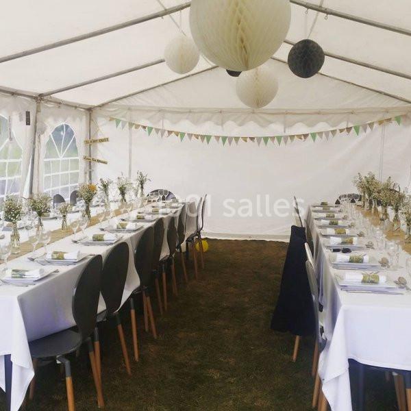 Tables dressées avec nappes blanches, décorations florales et guirlandes, sous une tente de réception.