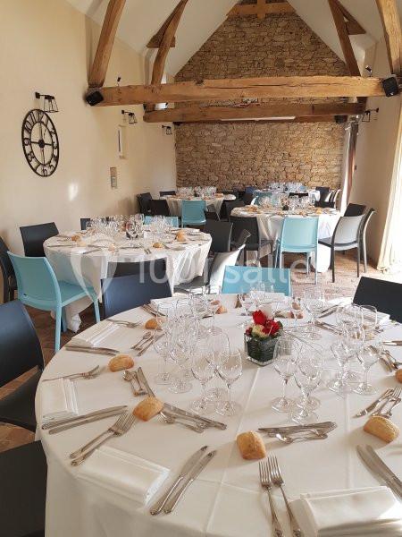 Salle de réception avec tables rondes dressées, nappes blanches, couverts, verres et décoration florale.