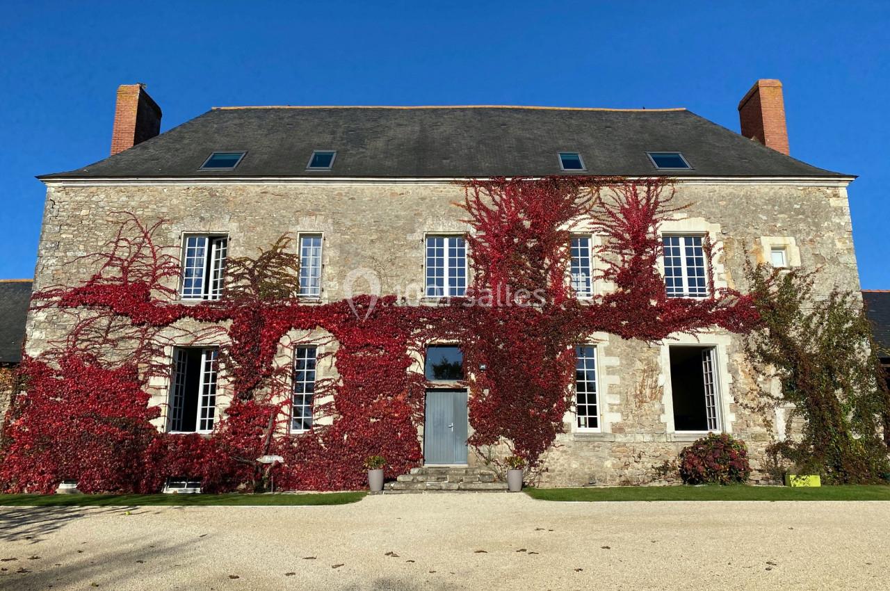 Façade d'une maison en pierre recouverte partiellement de vignes rouges, sous un ciel bleu clair.