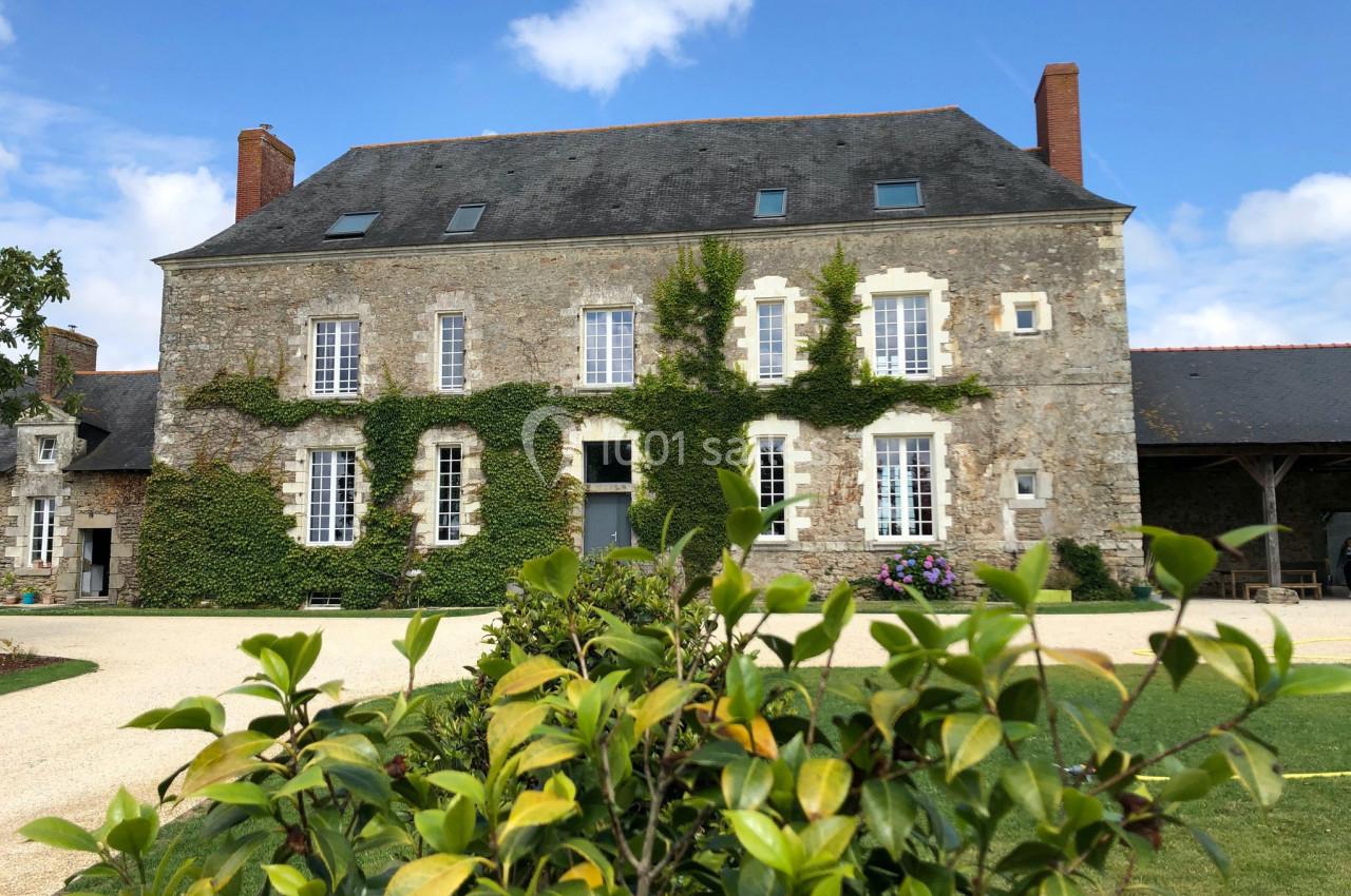 Façade d'une maison en pierre avec des volets blancs, des plantes grimpantes et un jardin au premier plan.