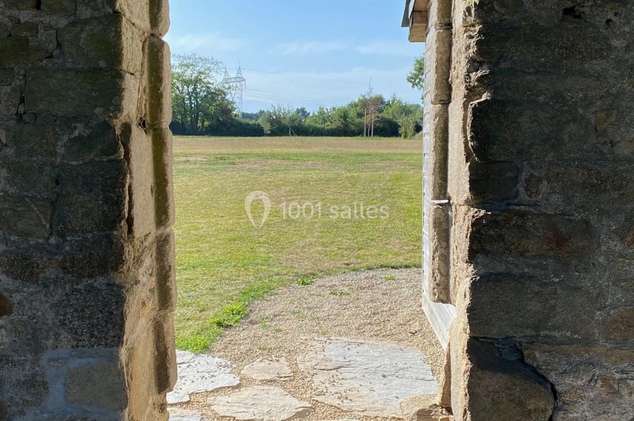 Vue à travers une porte en pierre ancienne donnant sur une pelouse ensoleillée et des arbres à l'arrière-plan.