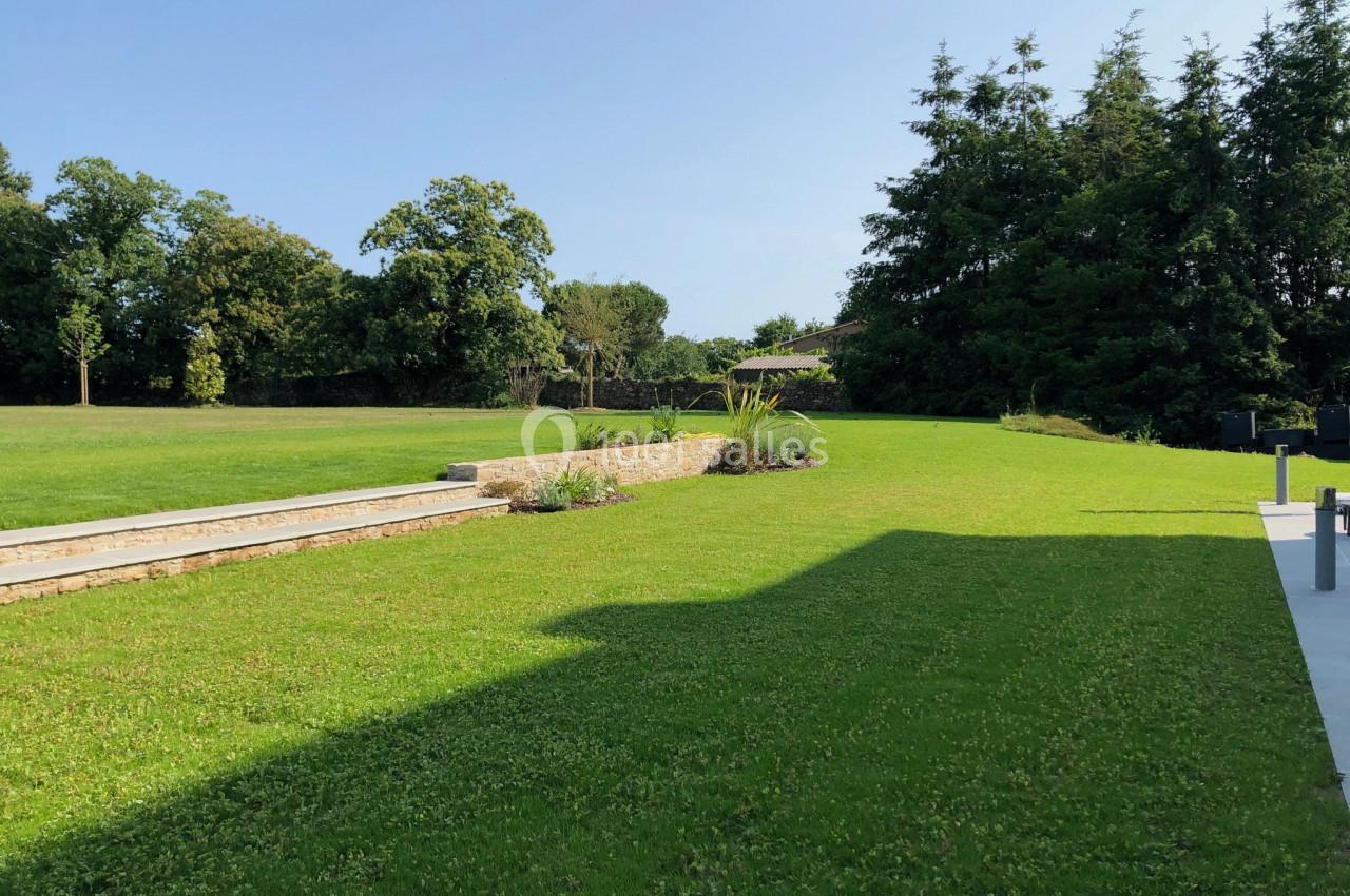Pelouse verdoyante avec quelques arbustes, bordée par des arbres et un muret en pierre sous un ciel dégagé.