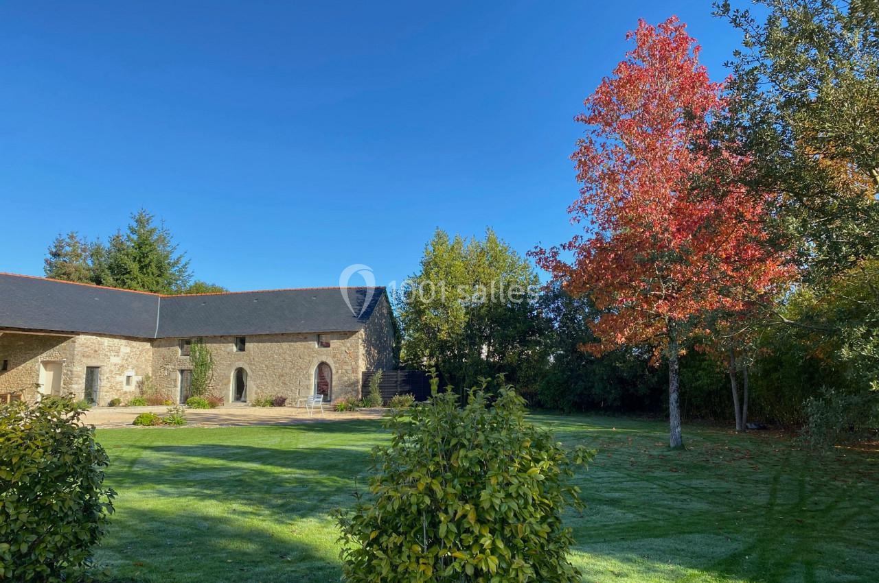 Cour verdoyante avec pelouse, arbres aux feuilles rouges et bâtiment en pierre sous un ciel bleu clair.