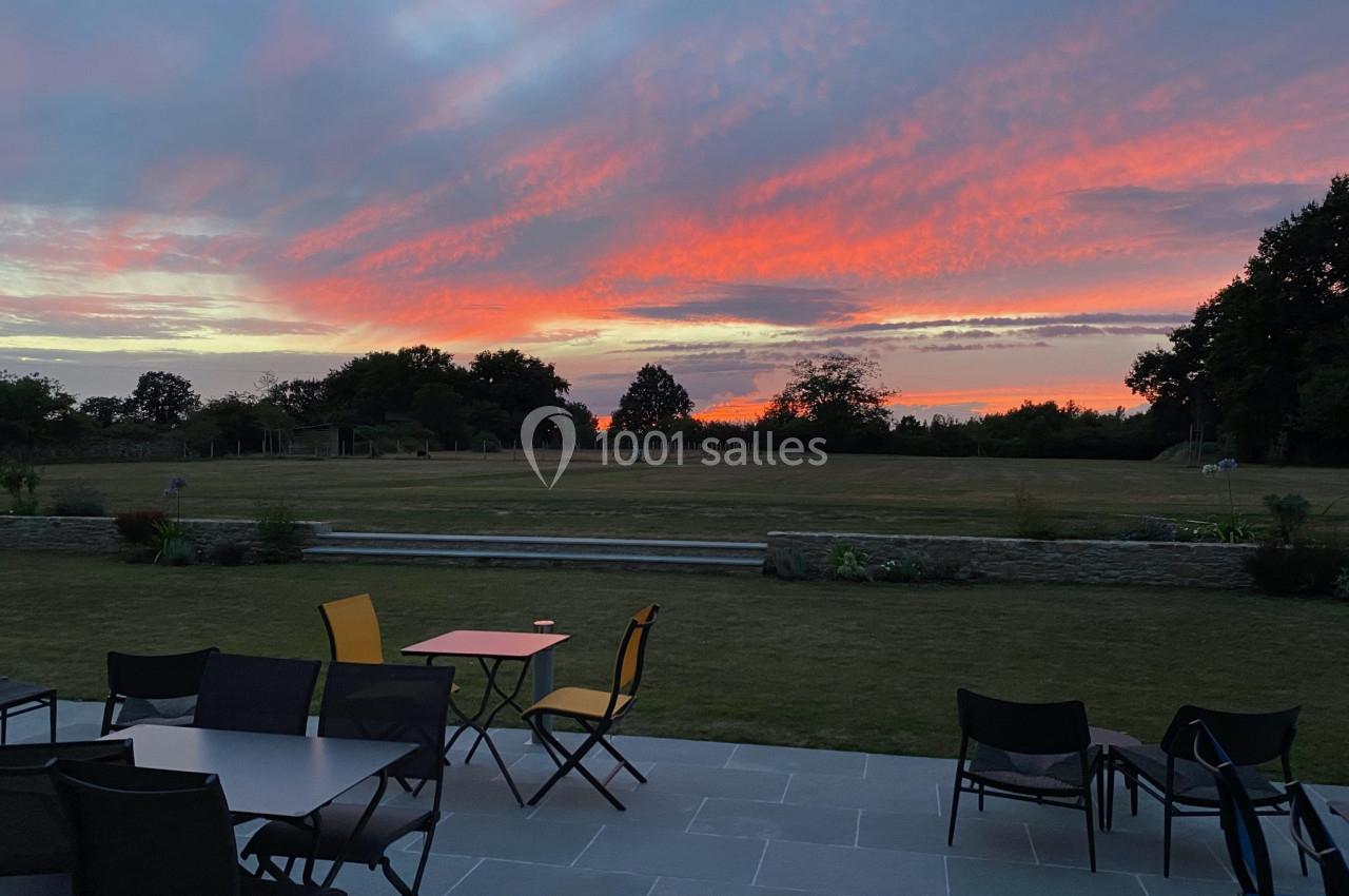 Ciel aux teintes roses et orangées au coucher du soleil, vu depuis une terrasse avec des tables et des chaises.