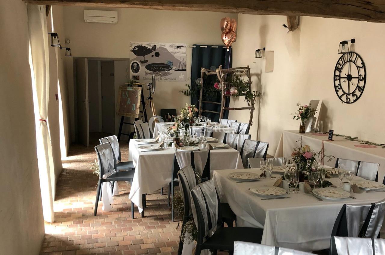 Salle de réception avec tables dressées, décoration florale et poutres apparentes sous un plafond en pente.