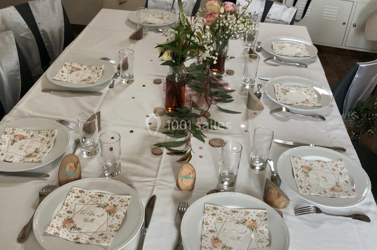 Table dressée pour un repas, décorée avec des fleurs, des menus imprimés et des marque-places personnalisés.