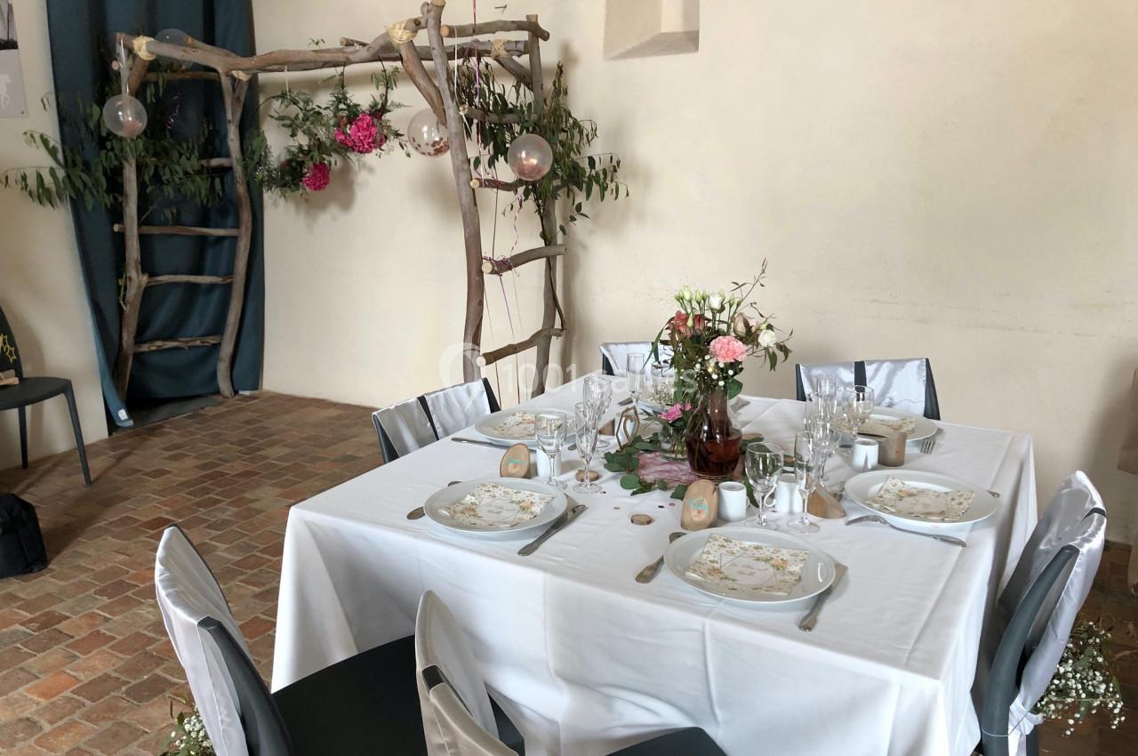 Table décorée pour un événement avec vaisselle élégante, fleurs et arche en bois ornée de feuillage et de fleurs.