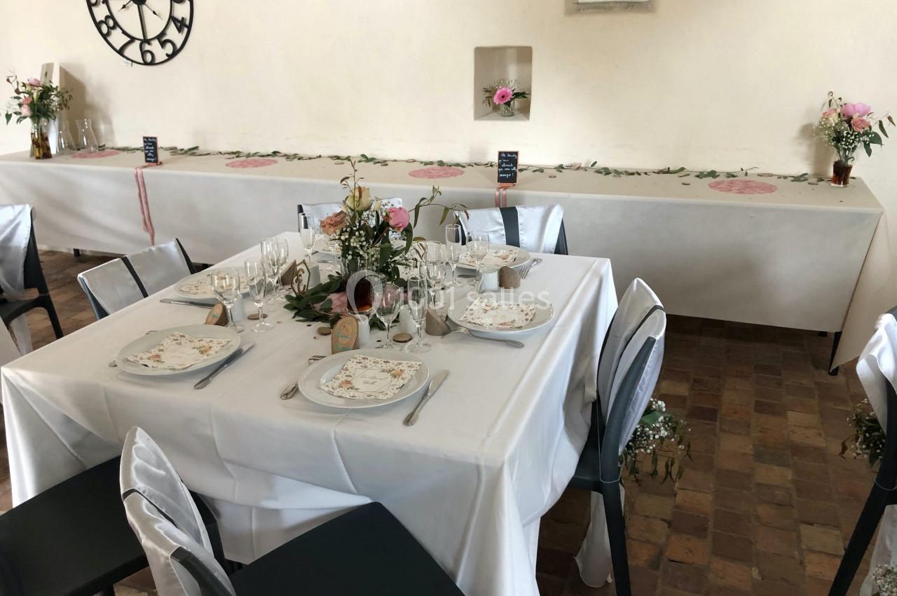 Table dressée pour un repas avec nappes blanches, vaisselle élégante, décor floral et chaises décorées.