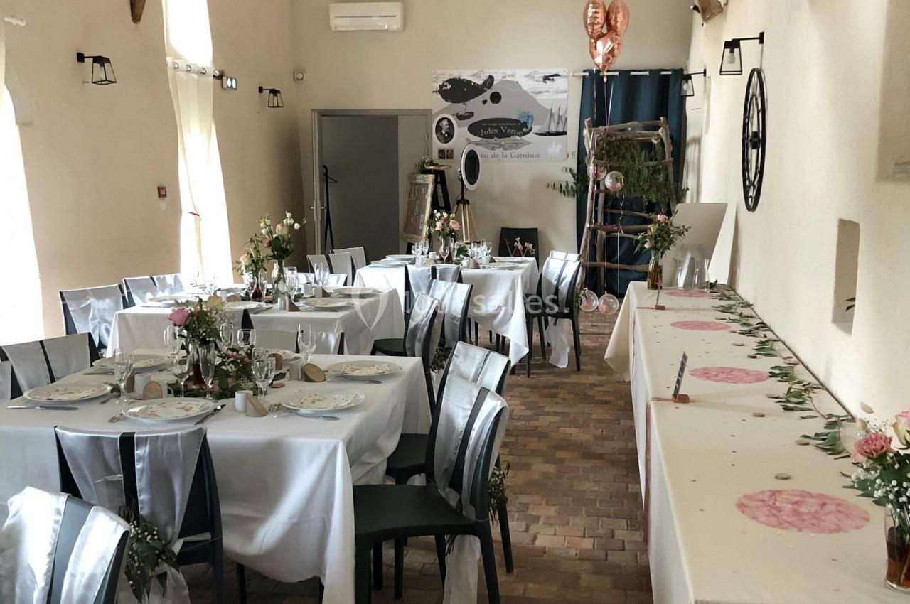 Salle de réception décorée avec des tables dressées, nappes blanches, fleurs et ballons en forme de cœur.