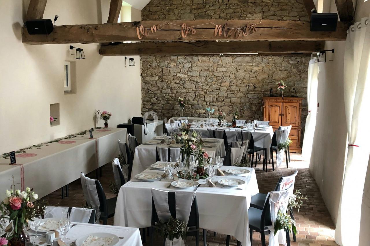 Salle de réception décorée pour un événement, avec tables dressées, poutres apparentes et mur en pierre.