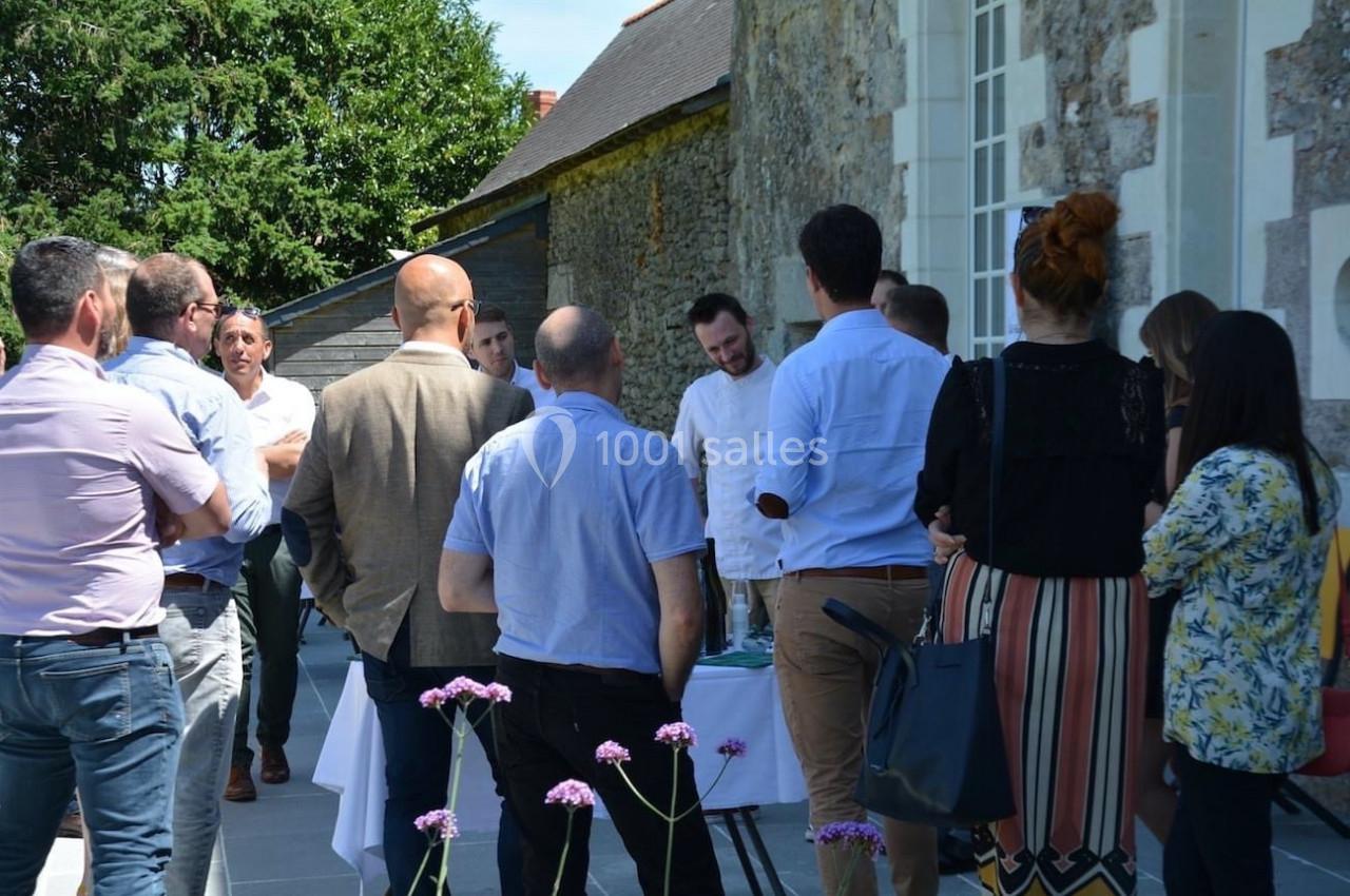 Un groupe de personnes discute à l'extérieur près d'un bâtiment en pierre, sous un ciel ensoleillé.