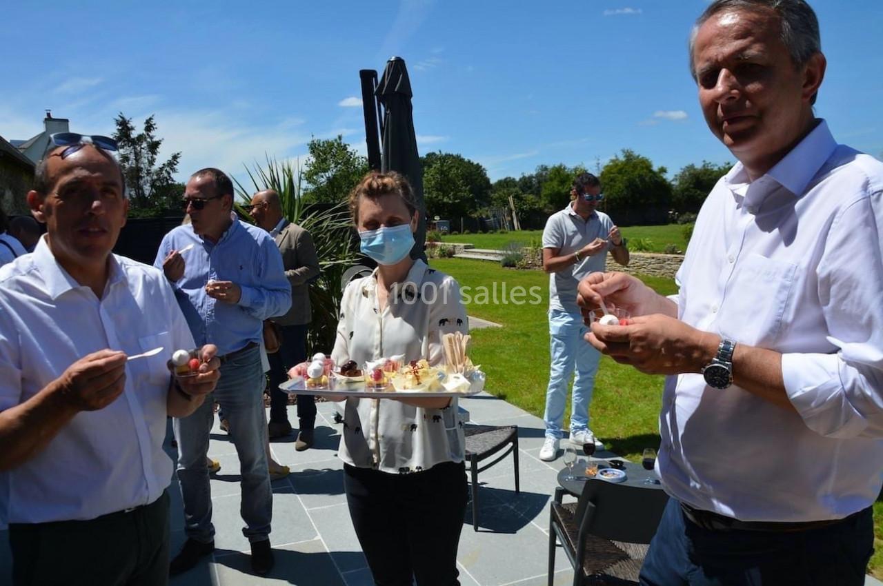 Des personnes dégustent des amuse-bouches en extérieur, sous un ciel ensoleillé, dans un jardin.