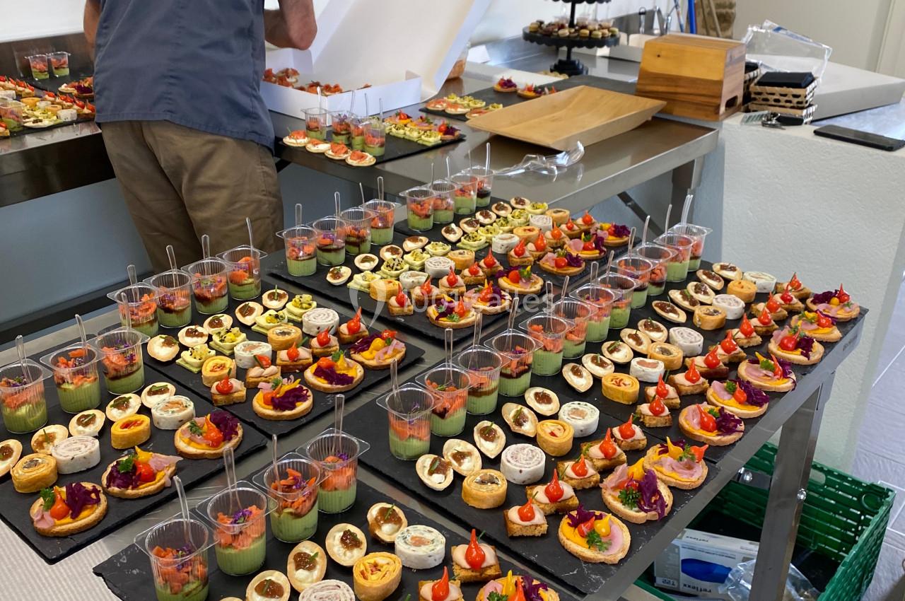 Un traiteur prépare des plateaux de bouchées apéritives variées dans une cuisine professionnelle.