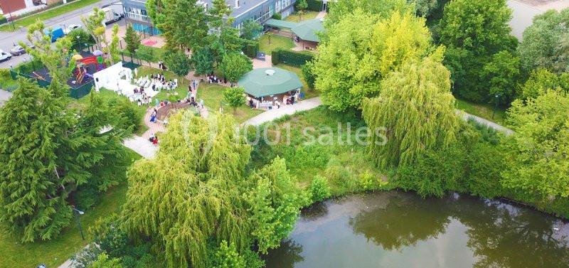 Vue aérienne d'un espace vert avec un étang, des arbres, une aire de jeux et des structures pour événements en plein air.
