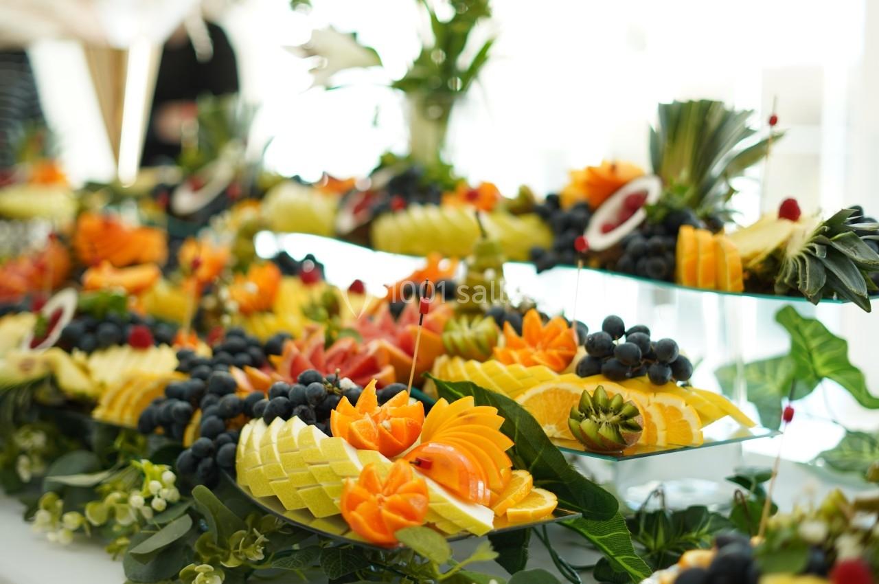 Plateau de fruits frais joliment découpés et disposés sur une table, avec des décorations végétales.