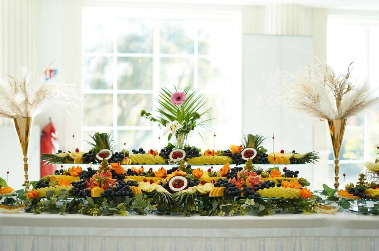 Buffet de fruits colorés et décoratifs avec des arrangements floraux dans un espace lumineux.