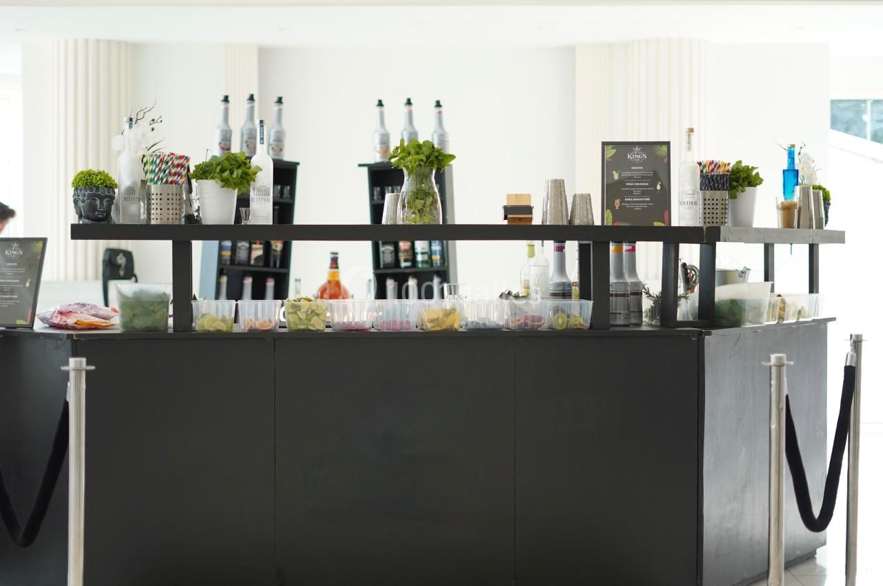 Bar moderne avec comptoir noir, décoré de plantes et bouteilles, proposant divers ingrédients et accessoires pour boissons.