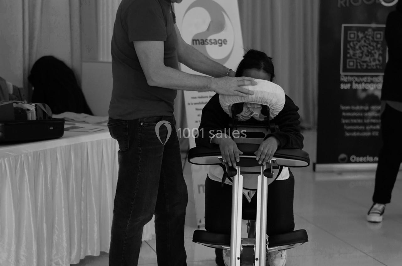 Un homme masse les épaules d'une personne assise sur une chaise ergonomique dans un espace intérieur lumineux.