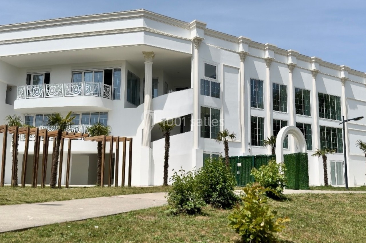 Bâtiment blanc moderne à deux étages avec colonnes, grandes fenêtres et espace paysager à l'avant.