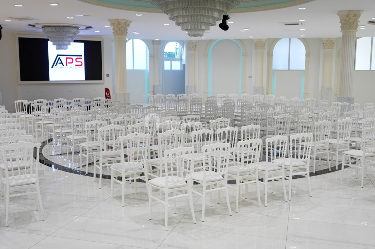 Salle lumineuse avec des chaises blanches alignées en cercle, écran allumé en arrière-plan.