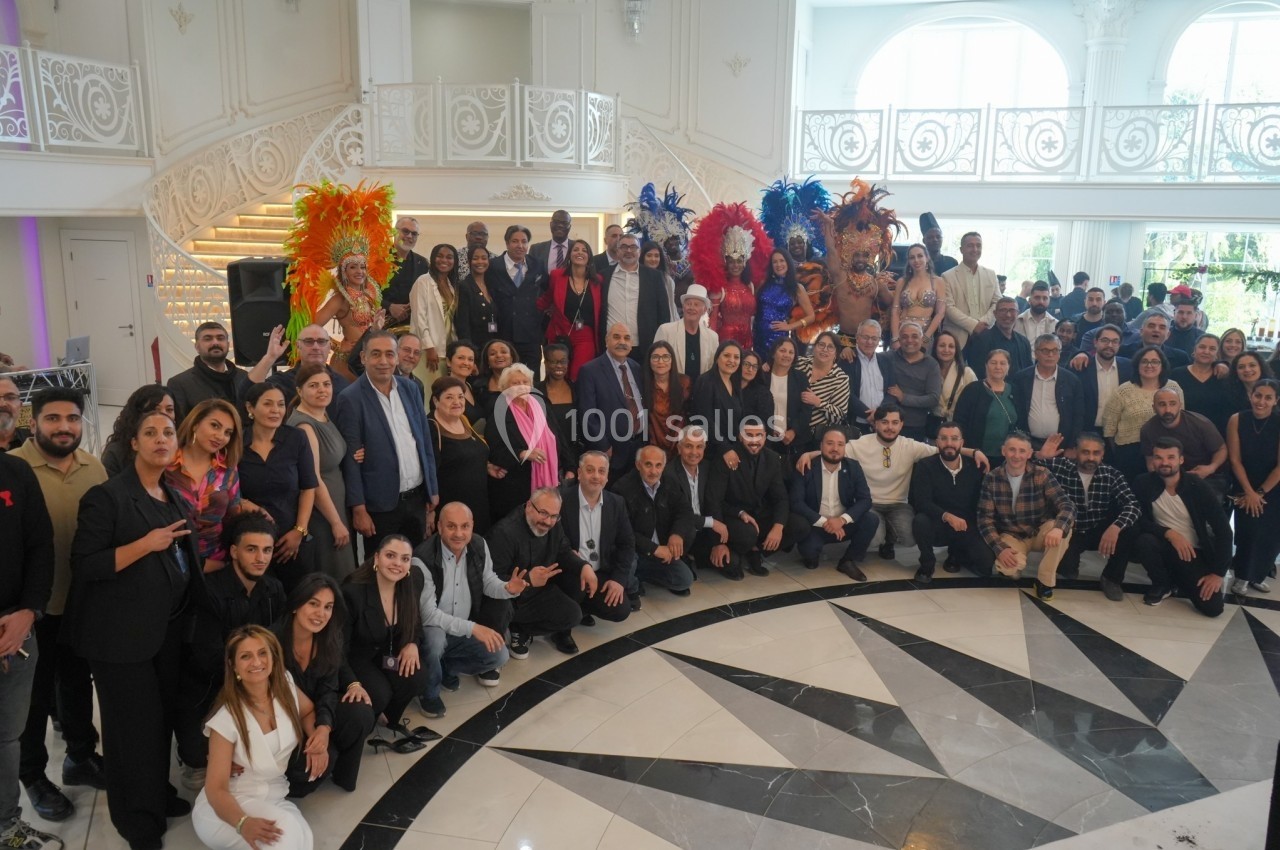 Groupe de personnes posant dans une salle élégante, avec des danseurs en costumes colorés à l'arrière-plan.