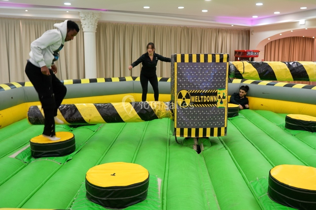 Deux personnes participent à un jeu d'équilibre sur une structure gonflable avec des obstacles rotatifs.