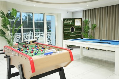 Table de billard bleu avec une queue et une bille, située dans une pièce lumineuse avec un baby-foot et de grandes baies…