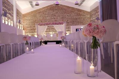 Salle de réception décorée pour un mariage, avec tables rondes, nappes blanches et guirlandes lumineuses au plafond.